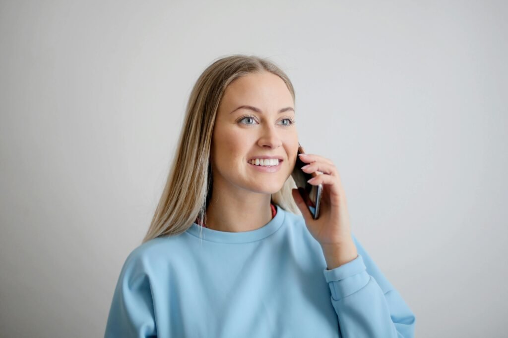 Cheerful woman in blue top smiling while having a conversation on her smartphone.